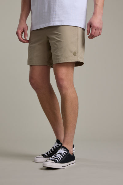 Only the lower half of a person is visible, wearing a white T-shirt, Barkers Davis Weekend Short in tan, and black Converse-style sneakers against a plain background.