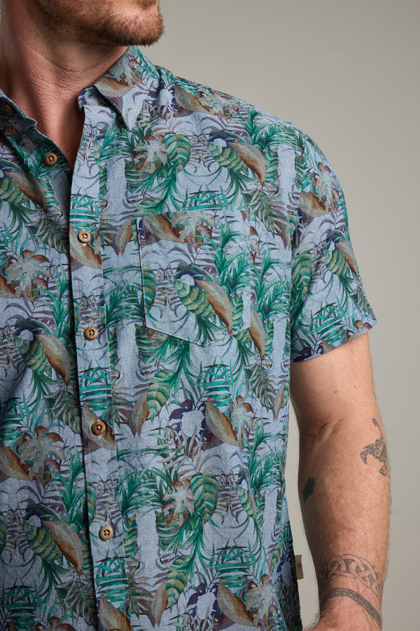 A man wears a Barkers Rockport Print Shirt with a vibrant tropical leaf design, ideal for summer parties. The focus is on the bold print and his tattooed arm, with his face partially out of frame.
