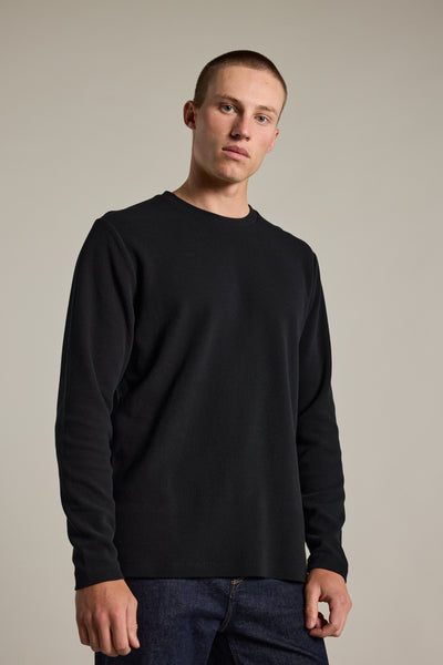 A young man with short hair wears the Barkers Avenue Waffle Crew in black and dark blue jeans, standing against a neutral background and looking directly at the camera with a neutral expression.