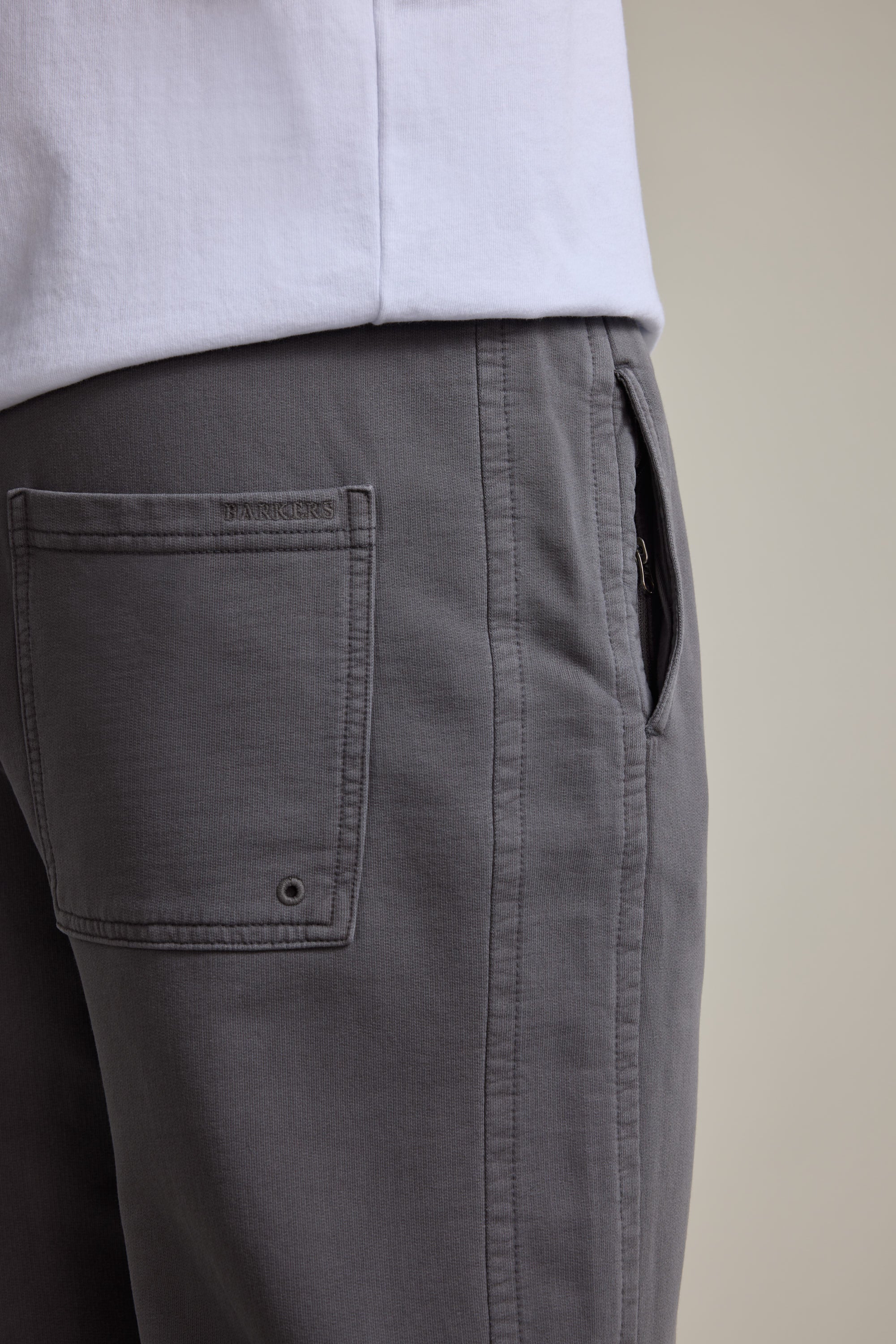 Close-up of a person wearing Barkers Organic Classic Print Track Pant in gray with a white shirt, highlighting the side and back pocket details of these 90s-inspired trackies.