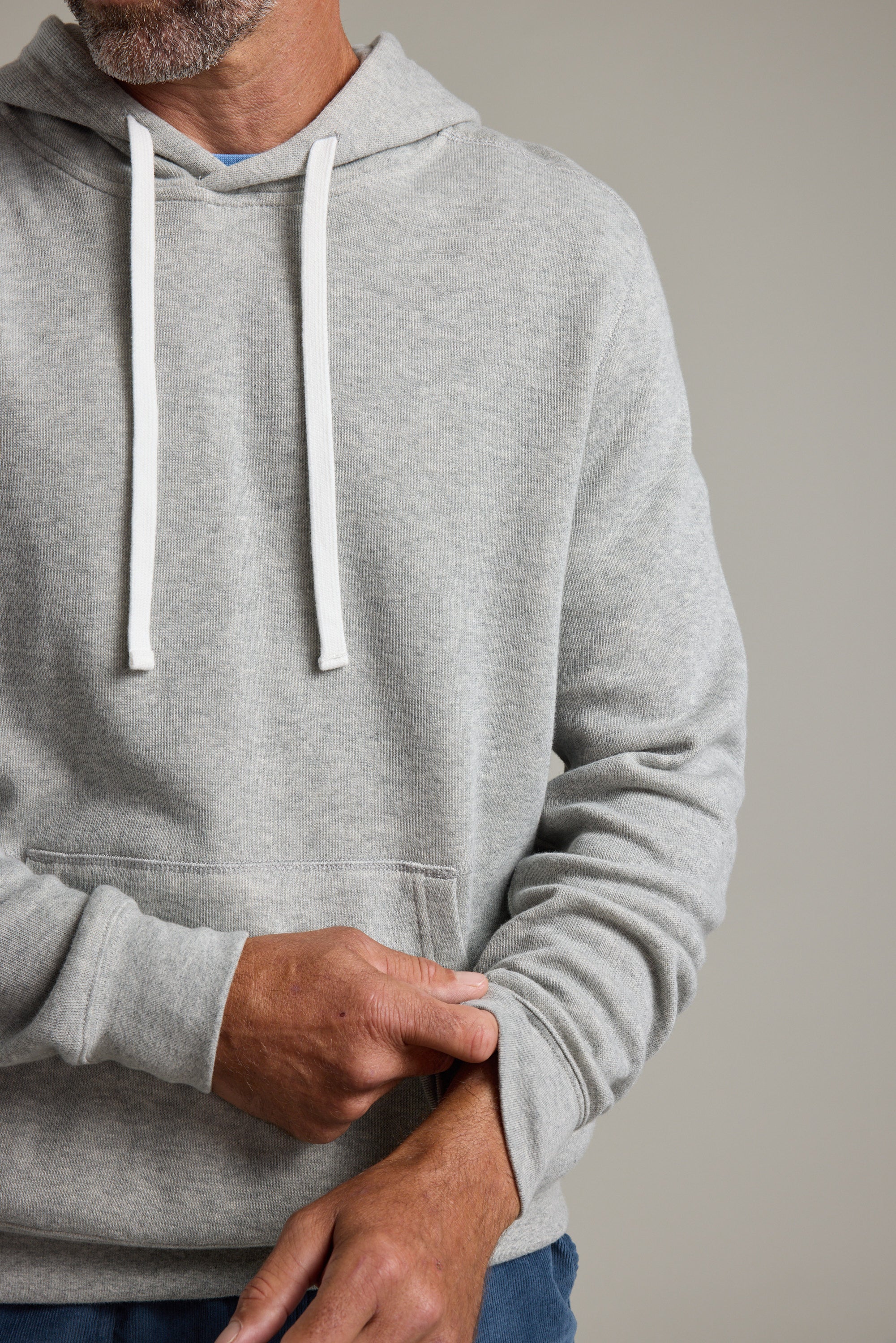 A person wears the Barkers Inlet Hoody in light gray organic cotton, pulling up one sleeve to reveal only their lower face, torso, and hands against a plain background.