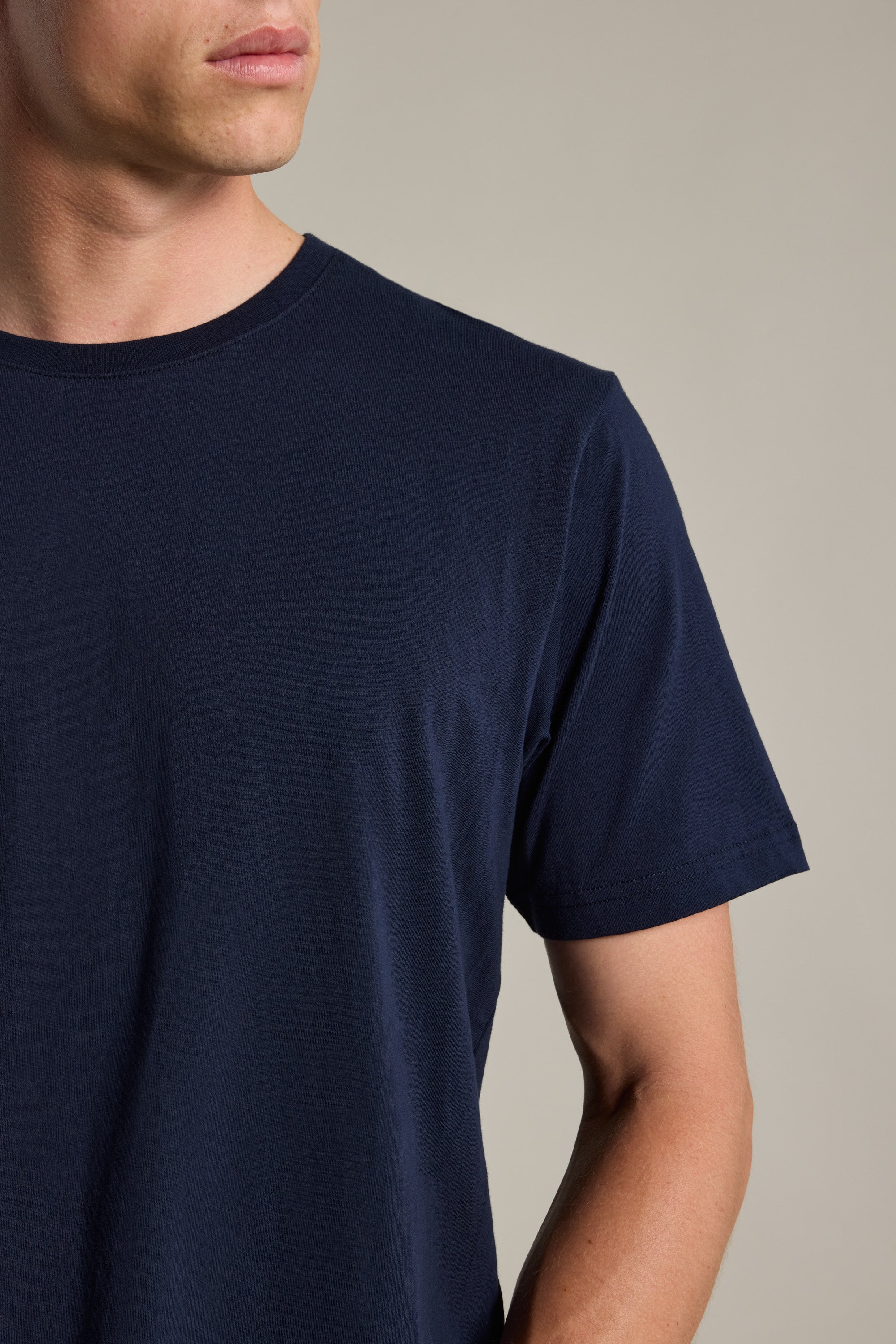 A man models the Barkers Organic Crew Tee in dark blue, made from organic cotton. Shown from shoulders to mid-arm and facing left against a neutral background, his face is partly visible and he doesn’t look at the camera.