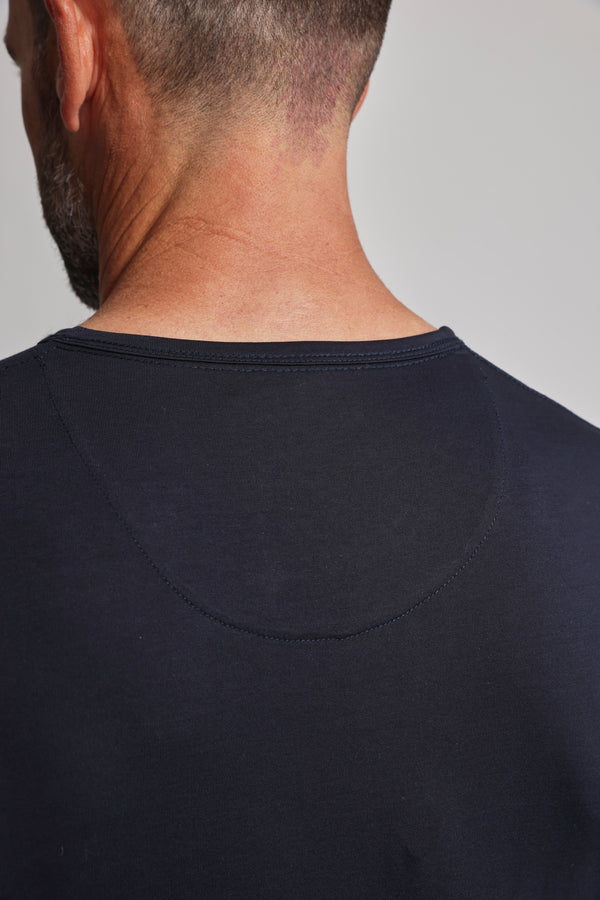 The image shows the back view of a man with short hair wearing the Barkers Linton Supima Tee, a dark navy blue crew neck made from mercerised Supima cotton, highlighting its neckline and stitching details.