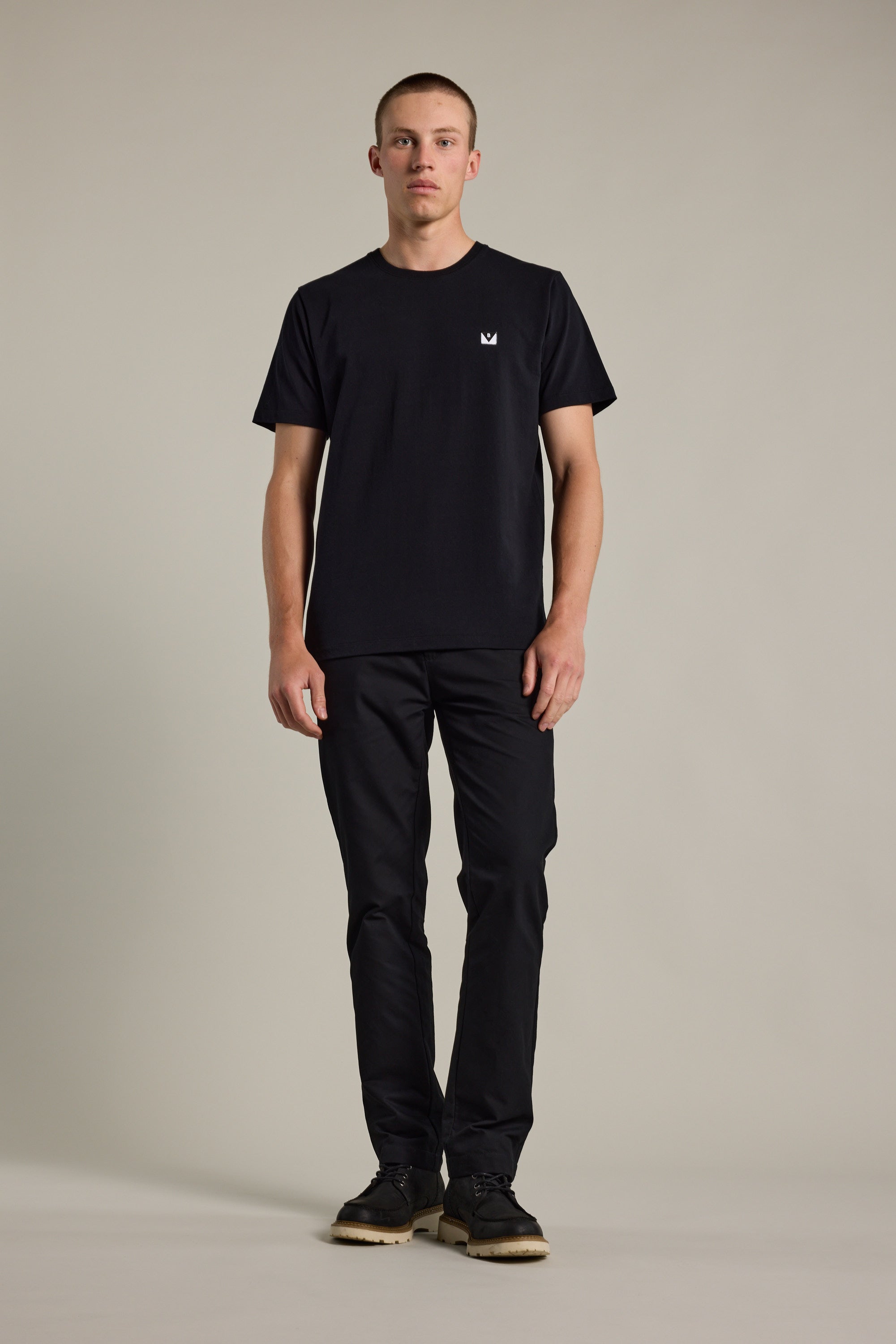 A man stands facing forward against a plain background, wearing the Barkers Newton Washed Tee—an oversized black box fit t-shirt with a small white logo on the chest—paired with black pants and black shoes.