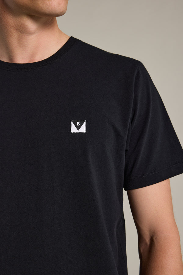 A person wears a Barkers Newton Washed Tee—an oversized, box-fit black t-shirt with a small ‘B’ patch on the left chest. The person's face is partially out of frame.