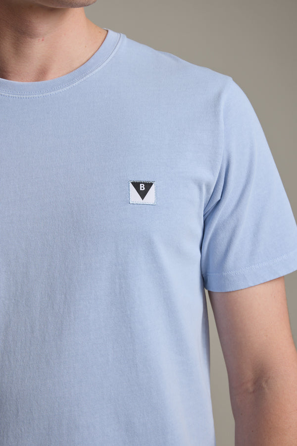 Someone is wearing the Barkers Newton Washed Tee, a light blue vintage-washed t-shirt with a small rectangular logo patch—a black triangle with the letter B—on the left chest.