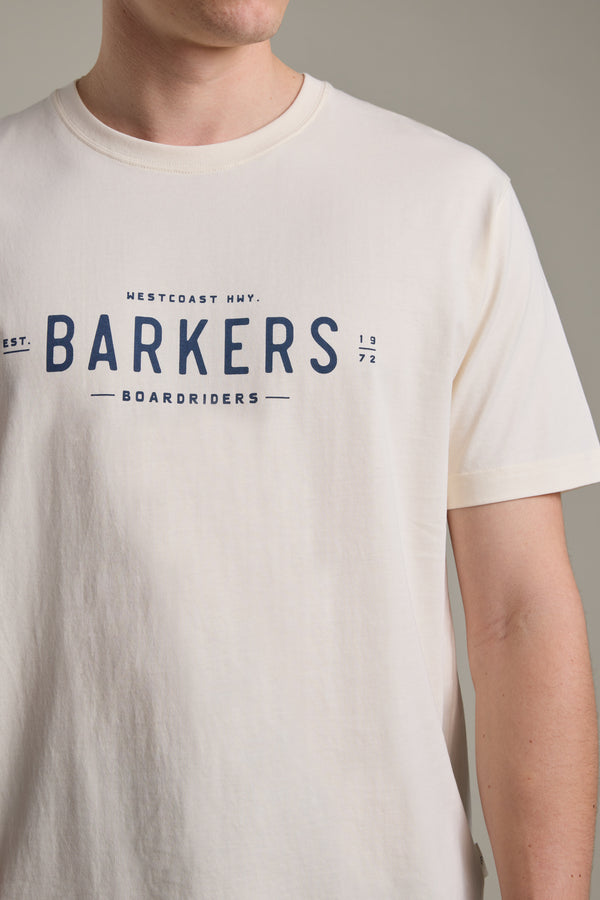Wearing a cream Barkers Boardriders Logo Tee, featuring bold branding and smaller WESTCOAST HWY. EST. 1972 details, the person's face is partly out of frame.