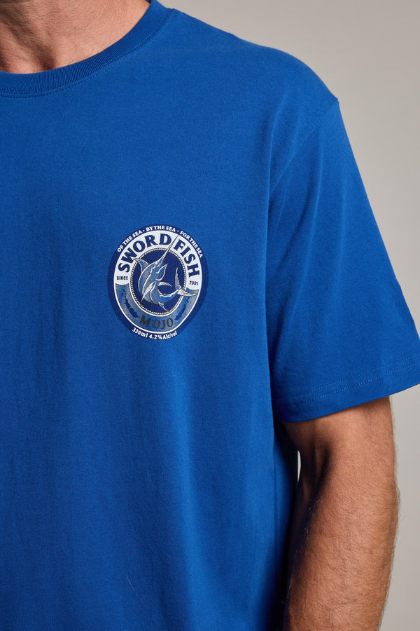 A person in a royal blue Swordfish Mojo Logo Tee by Swordfish Mojo, classic fit and organic cotton, featuring a circular chest logo with a swordfish and the phrase "Strength in the sea since 1983." Only the upper body is seen.