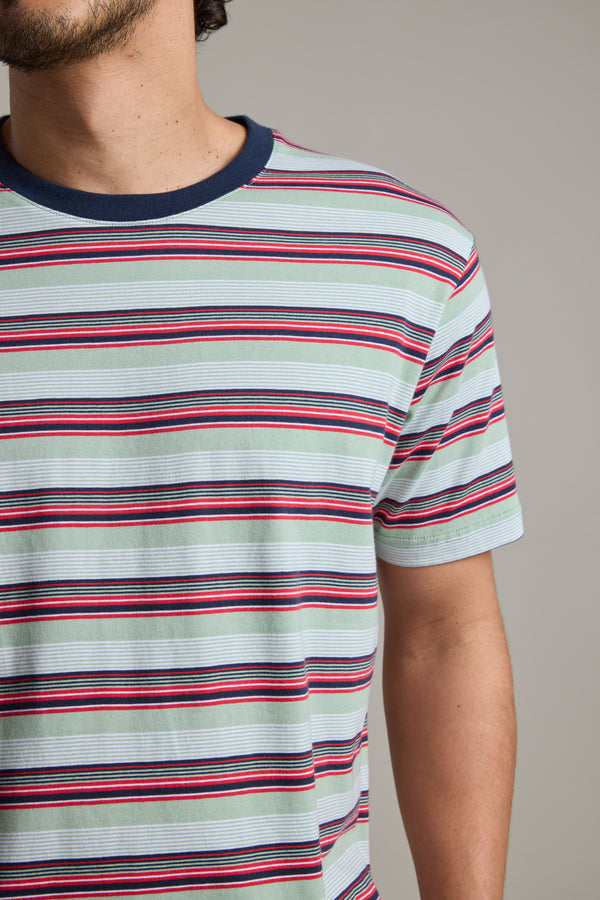 A person wearing the Barkers Alvin Stripe Tee—an organic cotton, short-sleeved shirt with red, black, and white horizontal stripes and a dark blue crew neck—shown from shoulders to waist, facing slightly left.