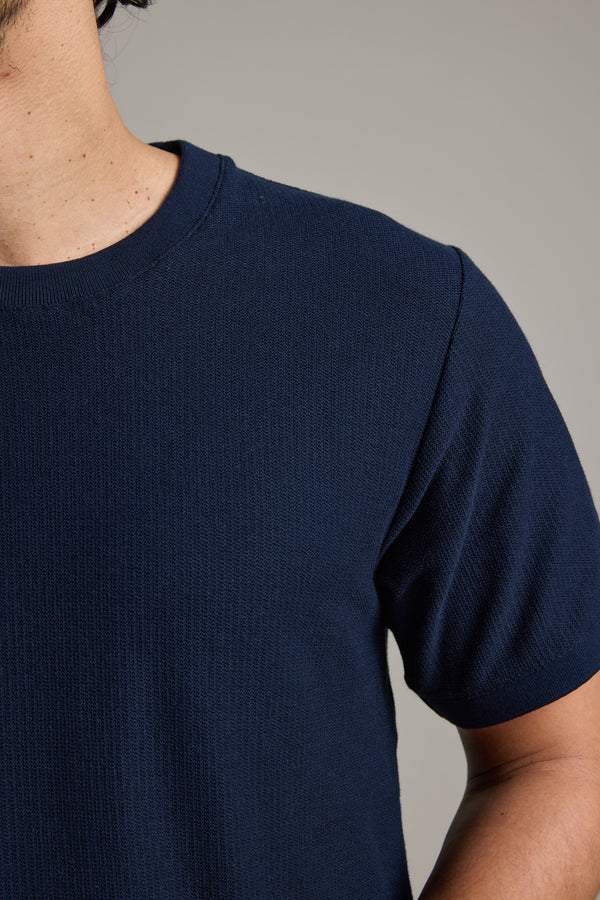 Close-up of a person wearing the Barkers Signature Knit Tee in navy blue, featuring ribbed cuffs. Only the neck, shoulder, and upper chest are shown against a neutral background, with the face partially out of frame.