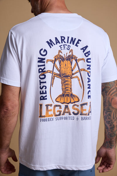 Someone wears the limited edition Legasea Crayfish Print Tee by Legasea, made from organic cotton, with a large crayfish graphic and “Restoring Marine Abundance, LEGASEA, Proudly Supported” on the back. Tattoos decorate their right arm.