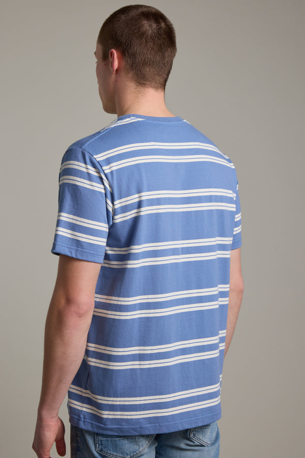 A person with short brown hair stands with their back to the camera, wearing the Barkers Northway Stripe Tee in blue and white stripes and light blue jeans, set against a plain gray background—ideal for summer style.