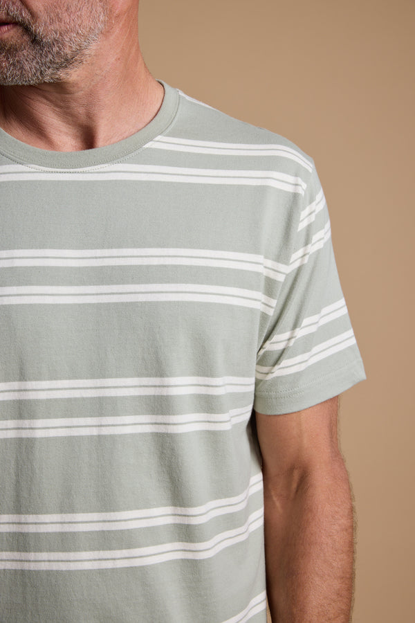 A close-up of a man wearing the Barkers Northway Stripe Tee in sage green and white, with only his lower face, neck, and upper torso visible. A stylish organic cotton piece—ideal for your summer wardrobe.
