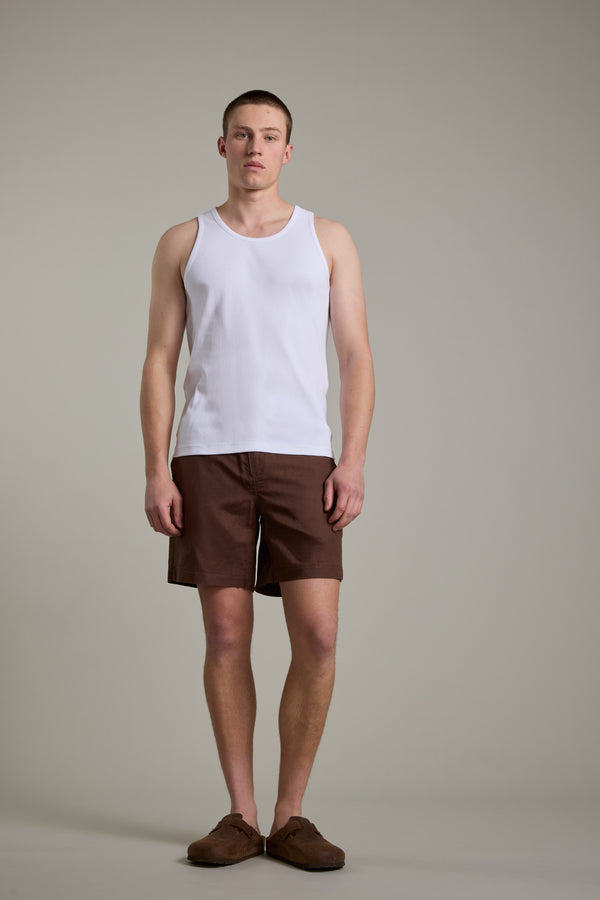 A person stands before a plain background wearing the Barkers Ribbed Singlet by Barkers in white, paired with brown shorts and shoes, looking at the camera with their arms relaxed at their sides.