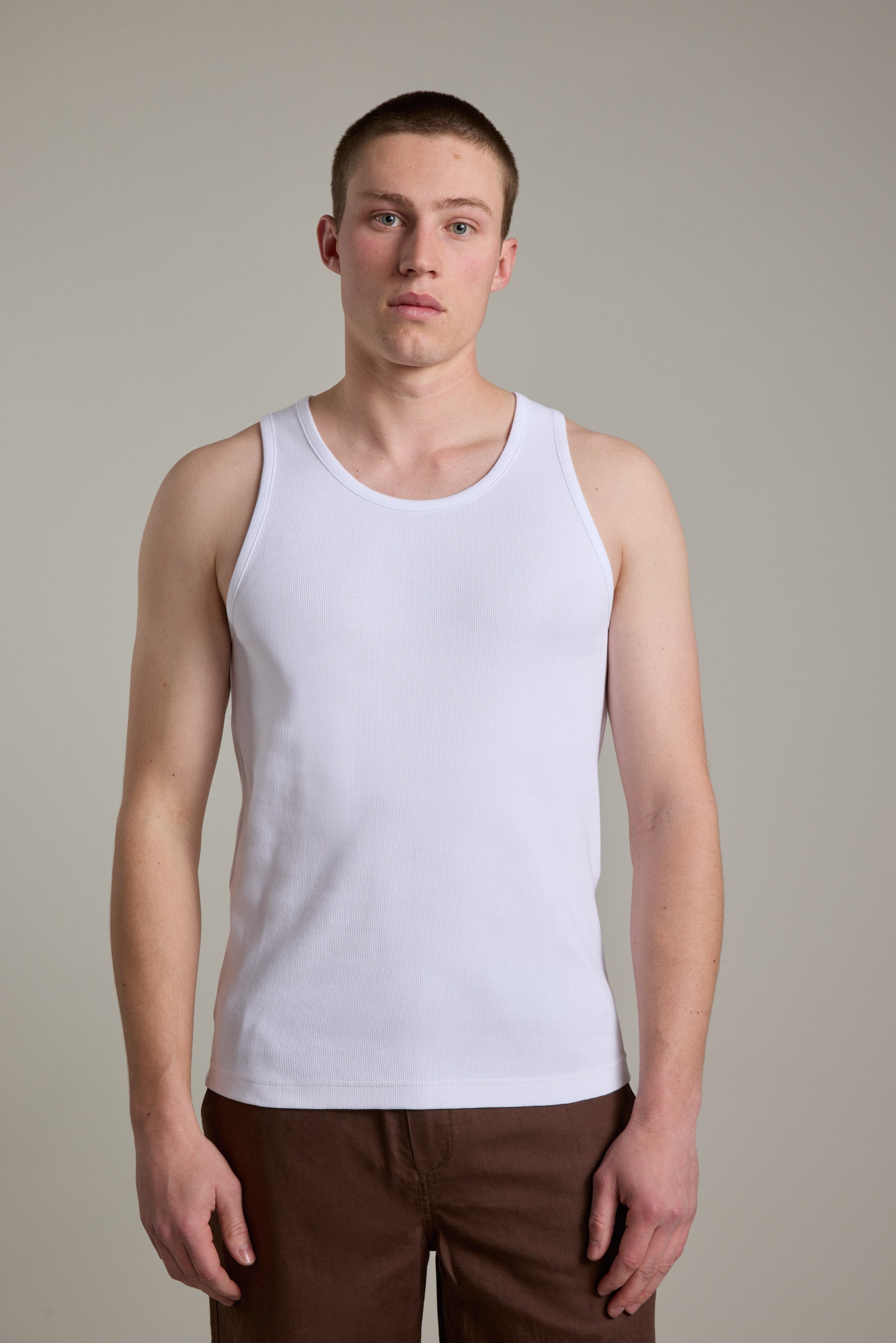 A young man with a neutral expression stands facing forward in Barkers brown pants and the Barkers Ribbed Singlet, set against a plain light gray background.