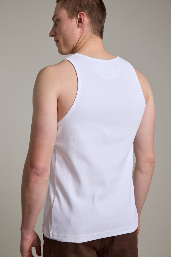 A man faces away from the camera, wearing the Barkers Ribbed Singlet by Barkers in white and brown pants, set against a plain light background.