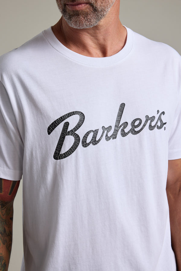 A man wears the Barkers Finely Tuned Print Tee, an organic cotton t-shirt with a vintage "Barkers" crackle print. Only the lower half of his face and upper torso are shown.