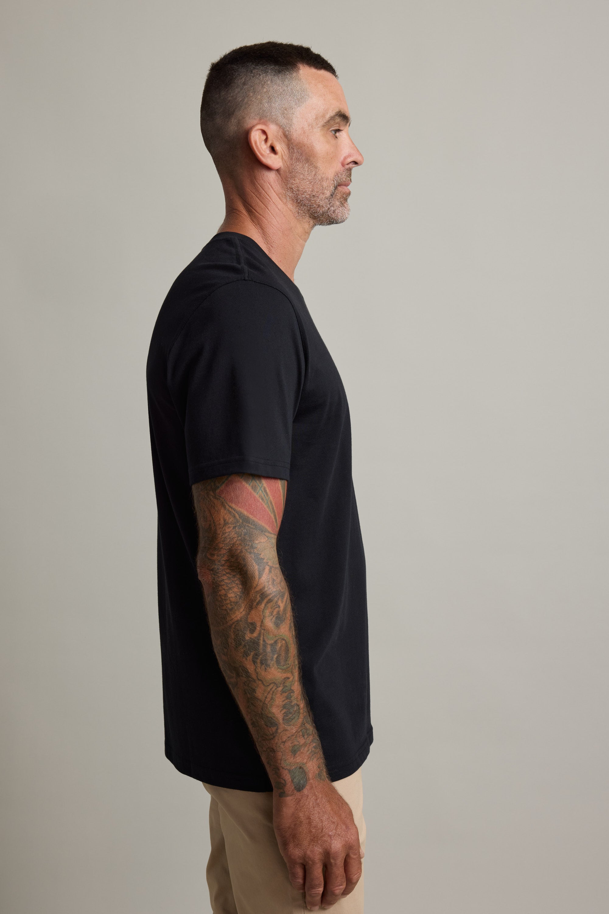 Man in a Barkers Good Earth Cotton Essential Tee and beige pants, showing arm tattoos in profile.