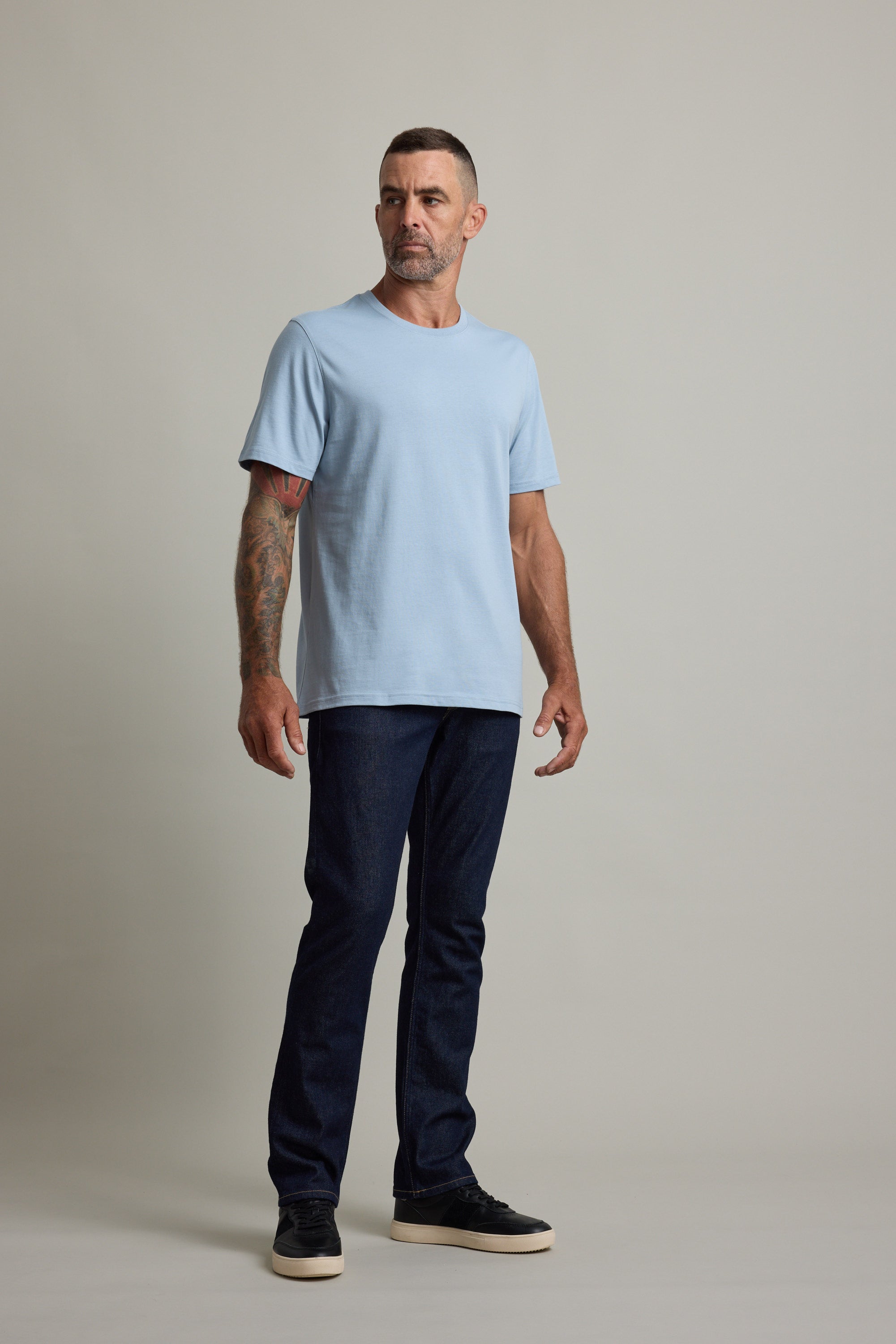 Man in a light blue Barkers Good Earth Cotton Essential Tee, dark jeans, and black sneakers.