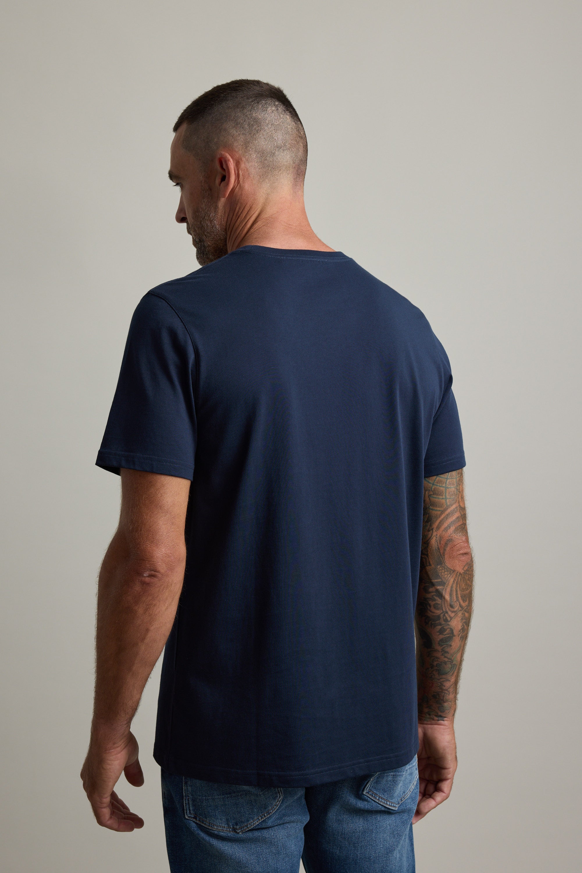 Man in a Barkers Good Earth Cotton Essential Tee and jeans, back to camera, neutral background.