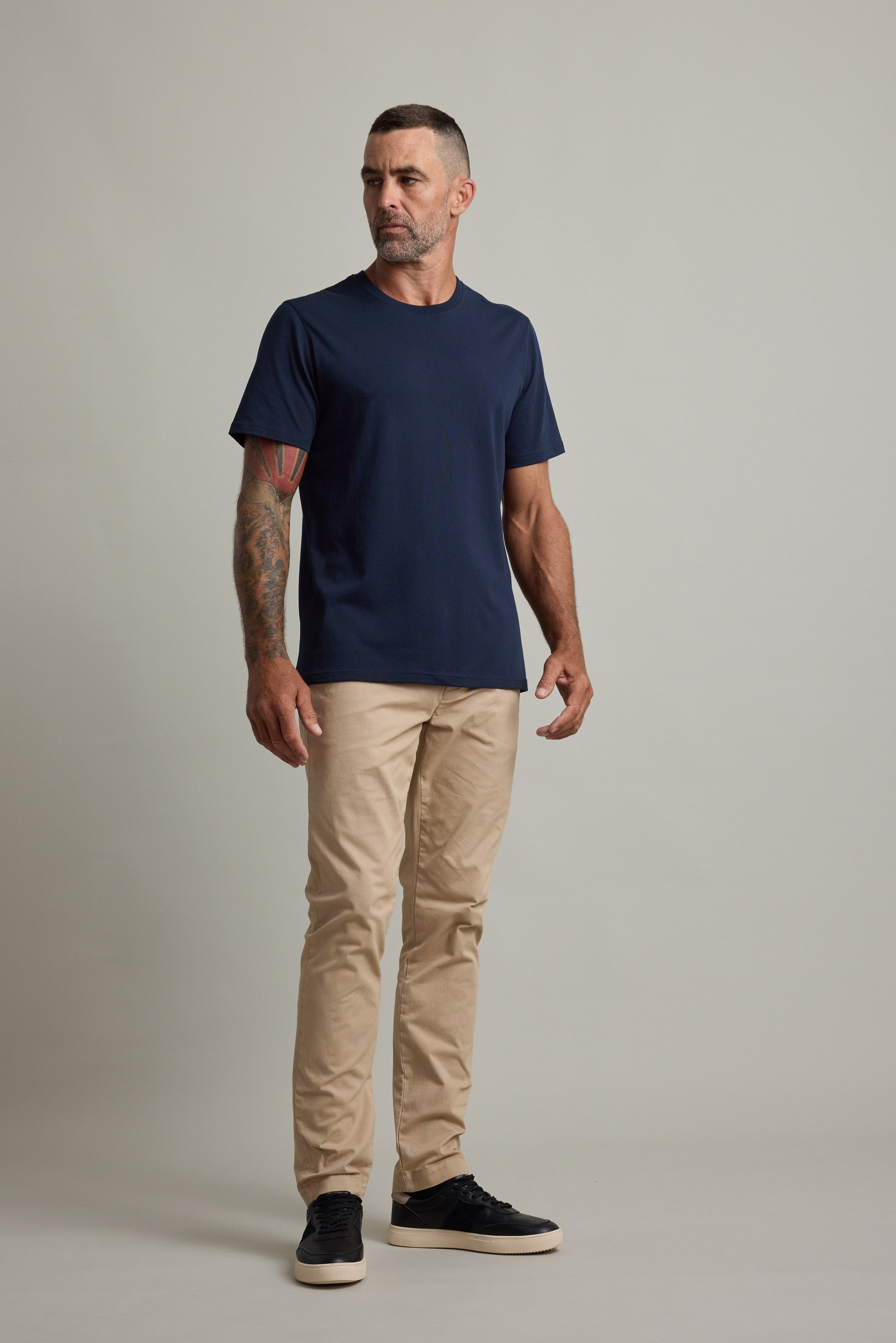 Man in Barkers Good Earth Cotton Essential Tee and beige pants stands against plain backdrop.