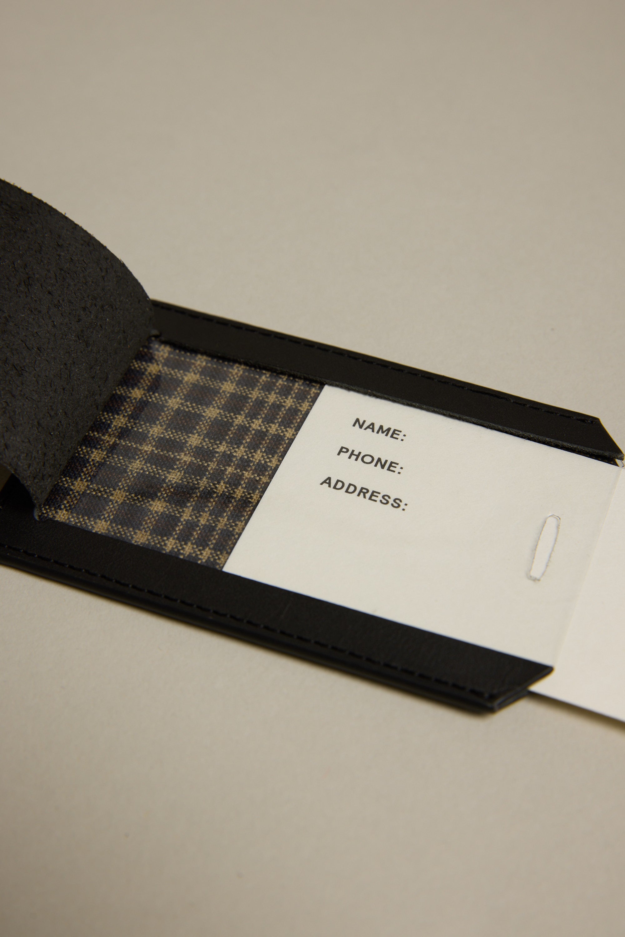 The Barkers Voyage Leather Luggage Tag is a black open leather tag with a plaid fabric interior and a white card for NAME, PHONE, and ADDRESS—perfect as a stylish travel accessory or corporate gift.