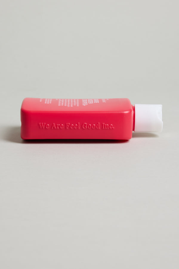 A pink rectangular bottle of Feel Good 50+ SPF Sunscreen by Other with a white flip-top cap lies on its side against a light beige background.