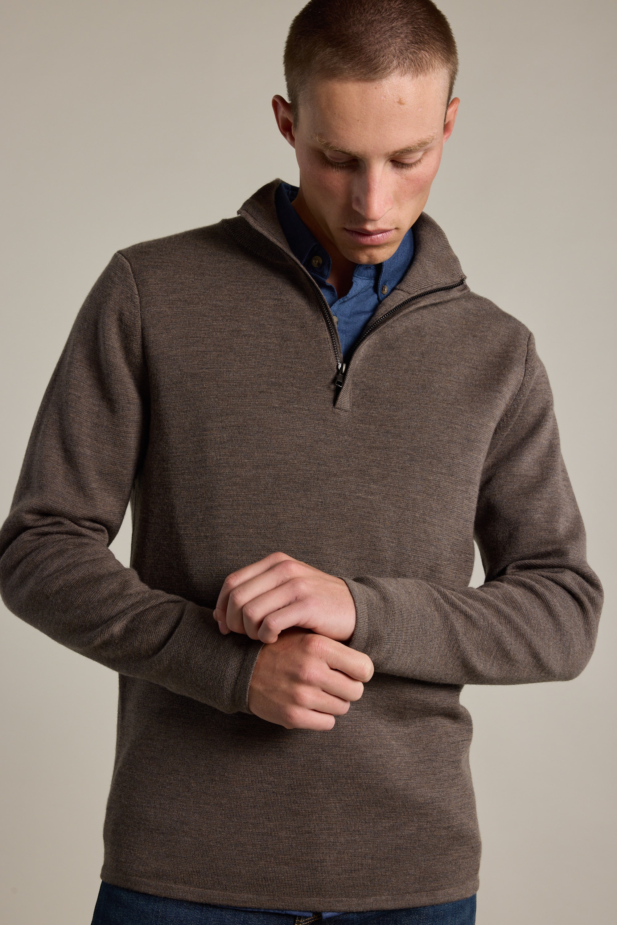 A person wears the Barkers Brandon ZQRX Merino 1/4 Zip sweater in brown over a blue shirt, adjusting their sleeve against a plain background—an ideal layering piece for versatile style.