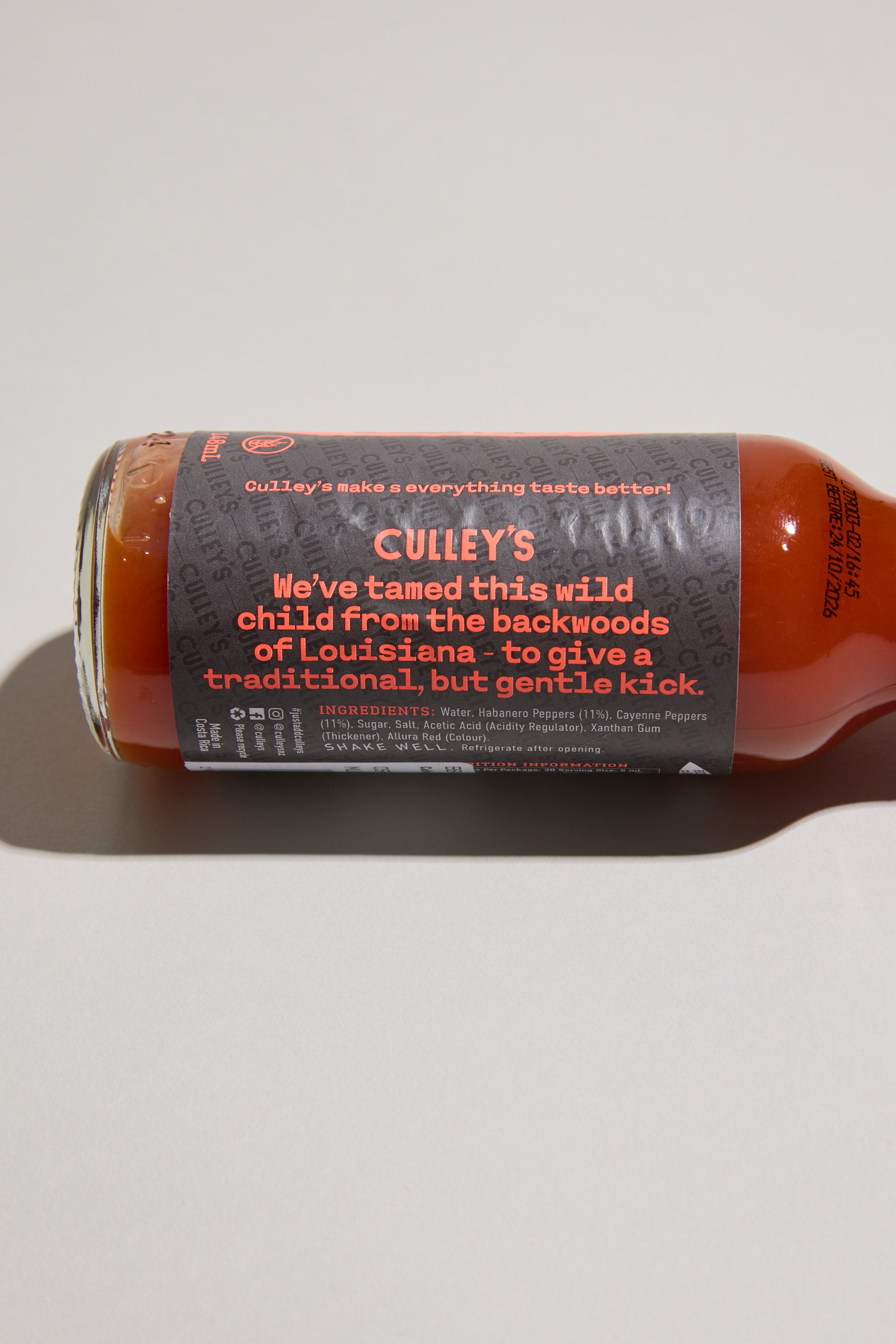 A bottle of Culley's Demure Habanero Hot Sauce rests on its side, showcasing a gray label with orange and white text that describes it as a wild child from Louisiana's backwoods with a gentle kick.