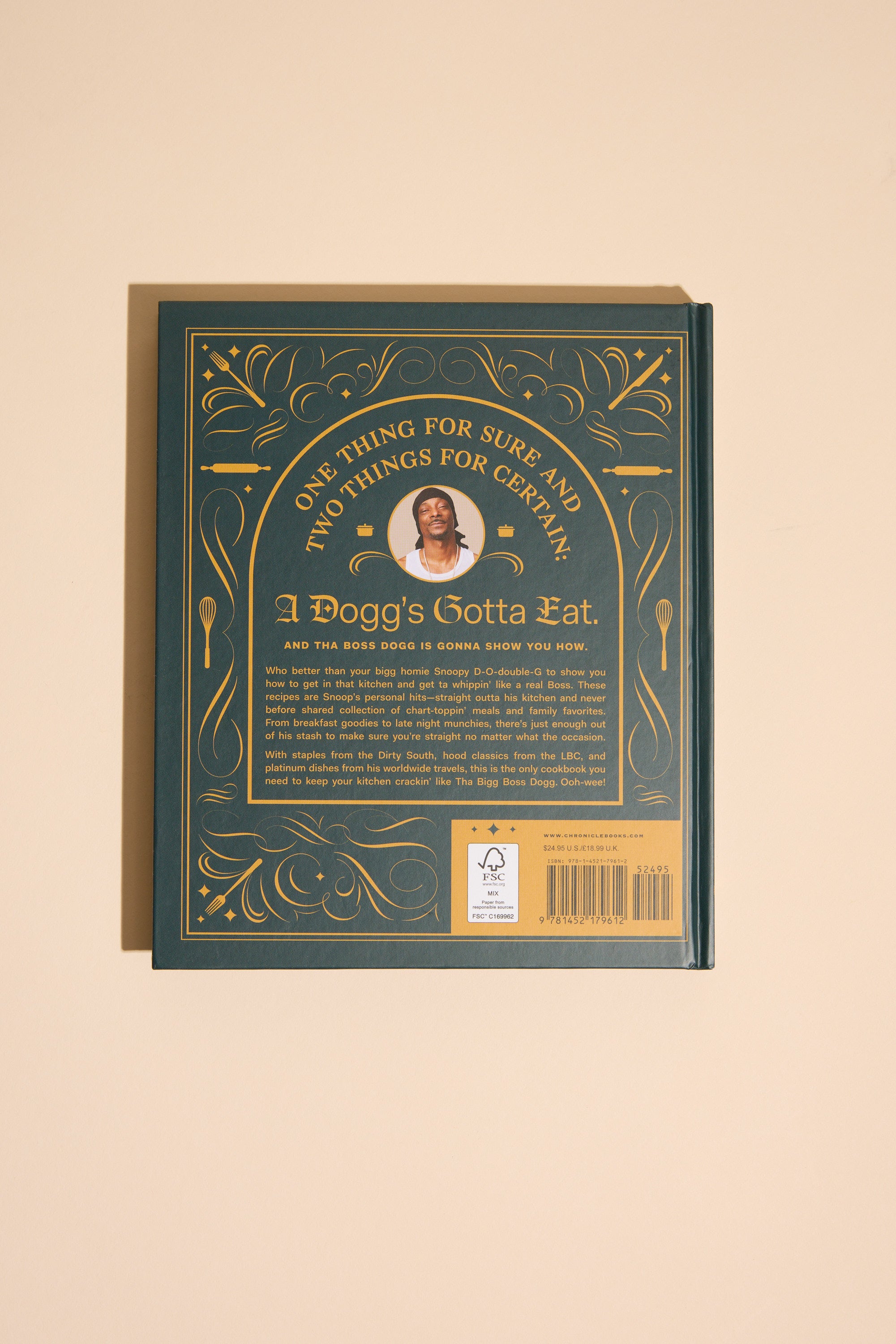 A dark green cookbook with gold accents and a central photo of a man, titled "From Crook to Cook" by Other, features cannabis-free Snoop Dogg recipes and is photographed on a beige background.