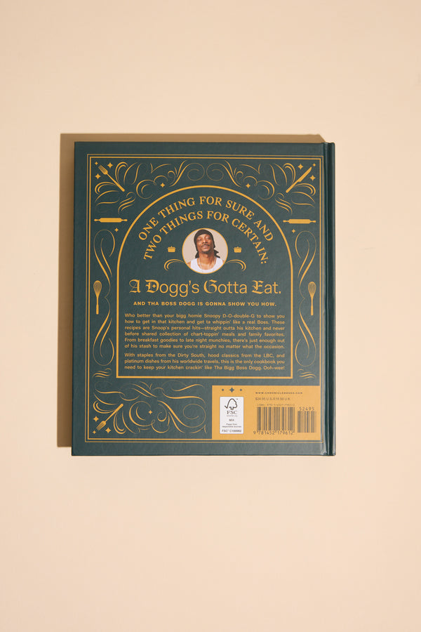 A dark green cookbook with gold accents and a central photo of a man, titled "From Crook to Cook" by Other, features cannabis-free Snoop Dogg recipes and is photographed on a beige background.
