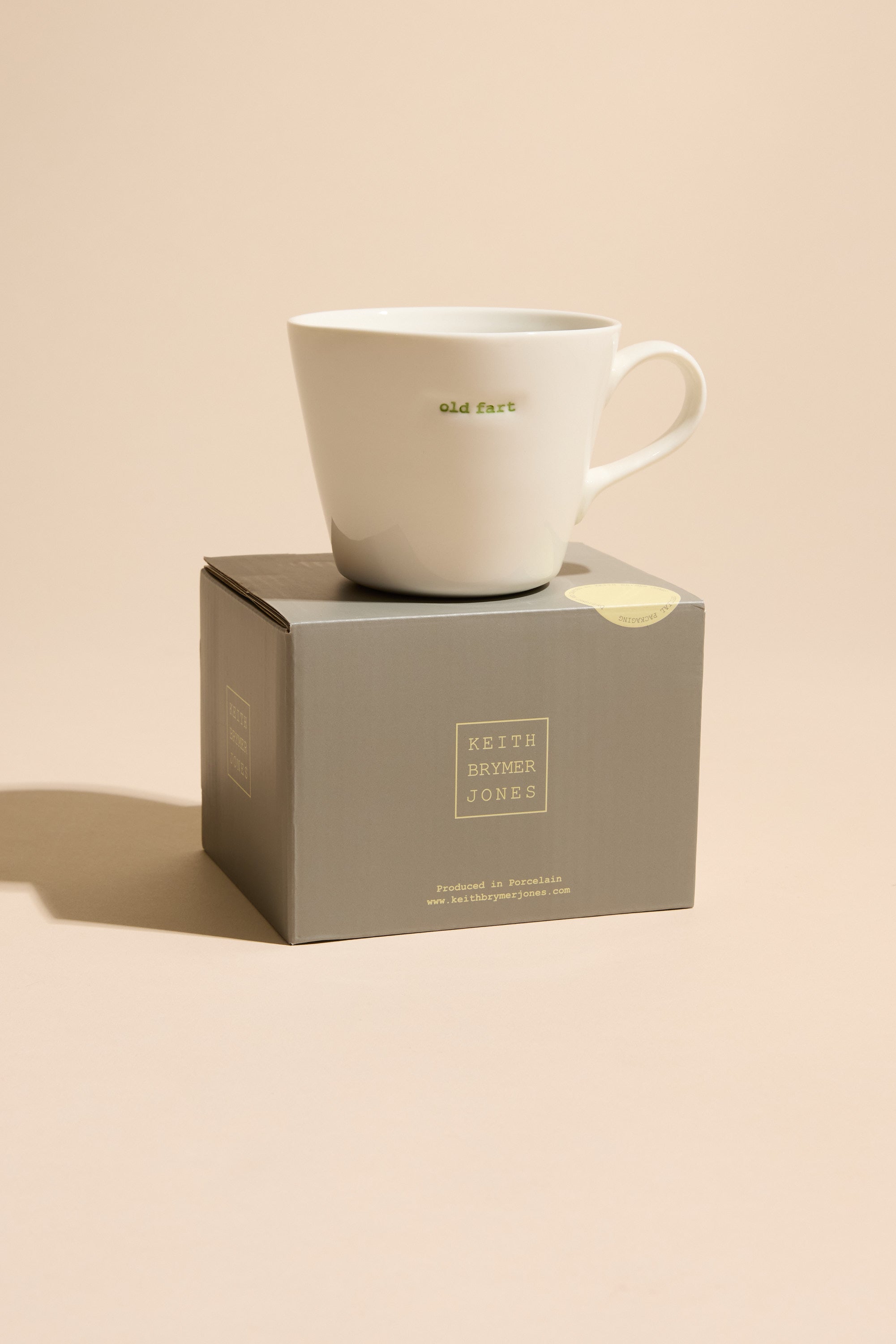 The Bucket Mug - Old Fart by Other features green lettering on a white mug, displayed atop a gray branded box—perfect as a fun gift for old fogey friends.