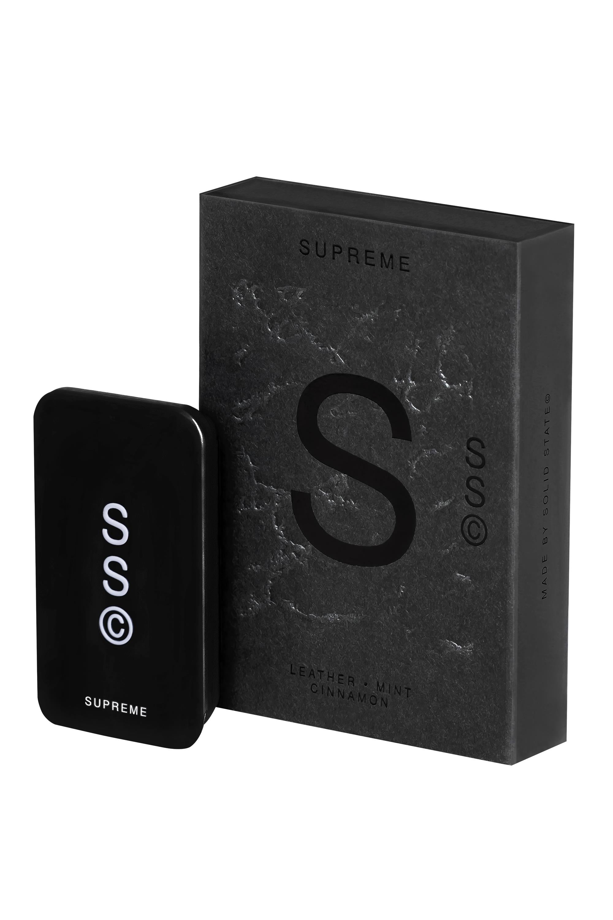 A sleek black rectangular tin labeled Solid State - Supreme stands next to a matching marble-textured box—this stylish solid cologne from Solid State offers a long-lasting Leather + Mint Cinnamon fragrance.