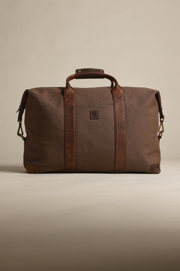 The Barkers Newman Canvas Weekender, a spacious brown men's bag with leather handles, accents, a front square logo, and sturdy metal hardware, stands upright against a neutral background.