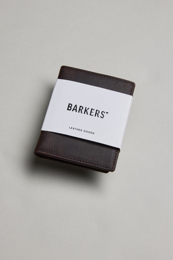 A Marlin Leather Slim Wallet by Barkers, dark brown and crafted from premium cowhide, is wrapped in a white paper band labeled "Barkers" and displayed on a plain light gray surface.