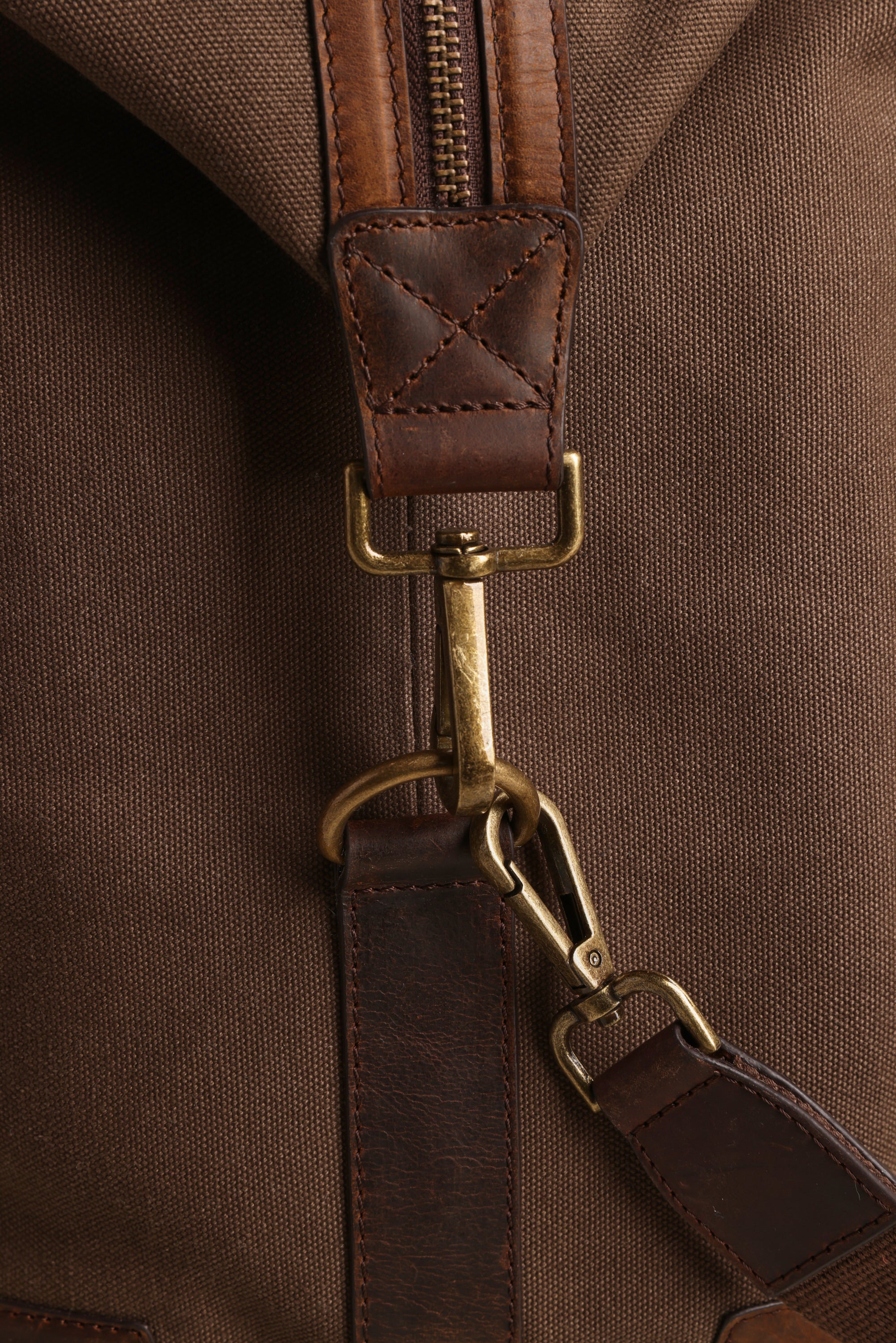 Close-up of the Barkers Newman Canvas Weekender, showing its brown canvas, leather strap with brass clasp and hardware, and detailed stitching. The texture and craftsmanship of this men's weekender are clearly visible.