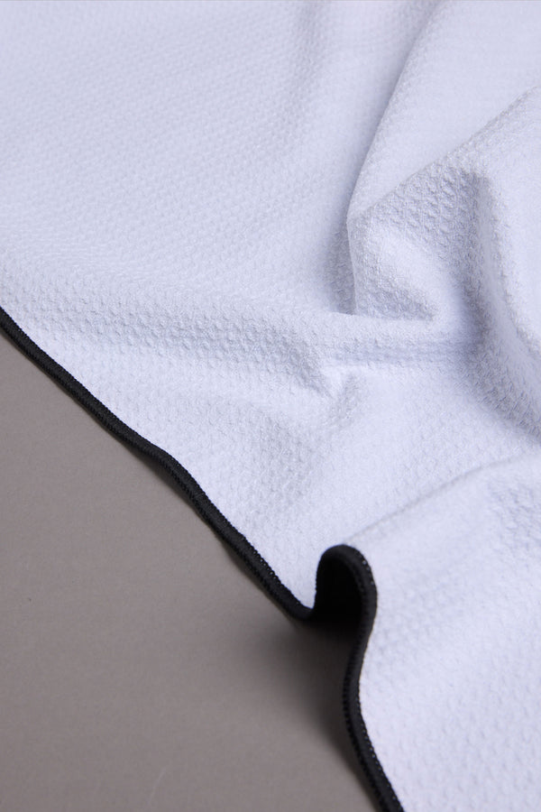 A close-up of the WearEver Utility Towel by WearEver, featuring white microfibre with black trim, draped over a smooth gray surface.
