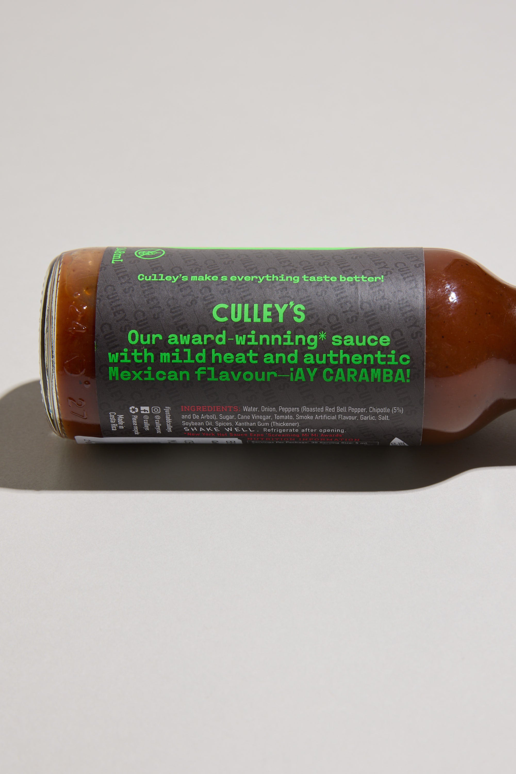 A bottle of Culley’s Cheeky Chipotle Hot Sauce rests on its side, showing a label that reads, “Our award-winning sauce with mild heat and authentic Mexican flavour – ¡AY CARAMBA!” Roasted red bell pepper is highlighted in the ingredients below.