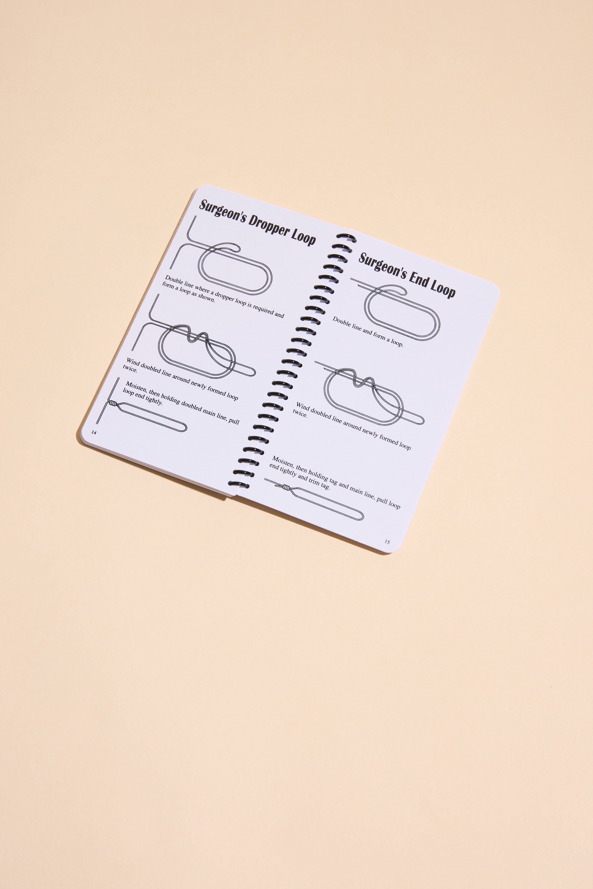 The "Fishing Knots" book by Other is open on a beige surface, showing black-illustrated step-by-step guides for tying the Surgeon’s Dropper Loop and Surgeon’s End Loop.
