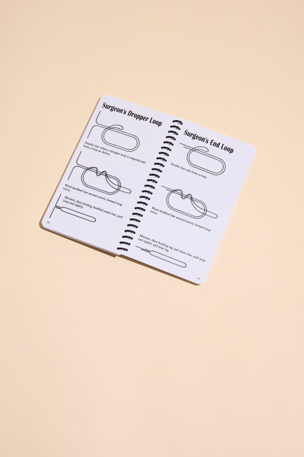 The "Fishing Knots" book by Other is open on a beige surface, showing black-illustrated step-by-step guides for tying the Surgeon’s Dropper Loop and Surgeon’s End Loop.