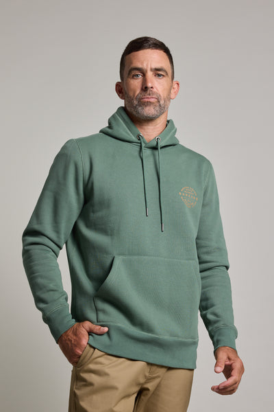 A man with short dark hair and a trimmed beard wears the Barkers Sunday Club Print Hoody in bottle green with a front pocket and tan pants, standing against a plain light gray background.