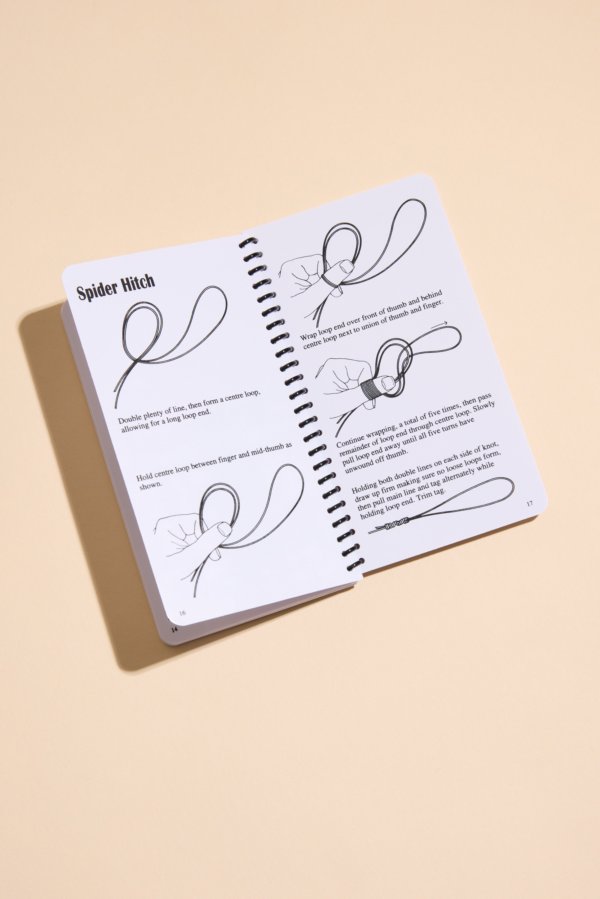 The open spiral-bound "Fishing Knots" book by Other rests on a beige surface, displaying illustrated step-by-step instructions and clear text for tying a Spider Hitch knot.