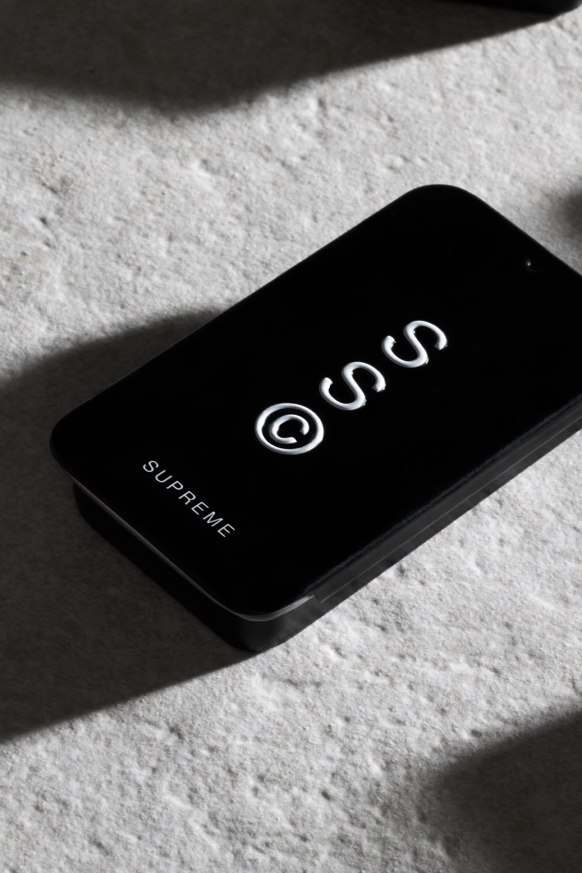 A black rectangular box labeled "Solid State - Supreme" by Solid State, featuring a white abstract lid design, suggests premium wax-based cologne. The packaging is displayed on a light textured surface with soft shadows.