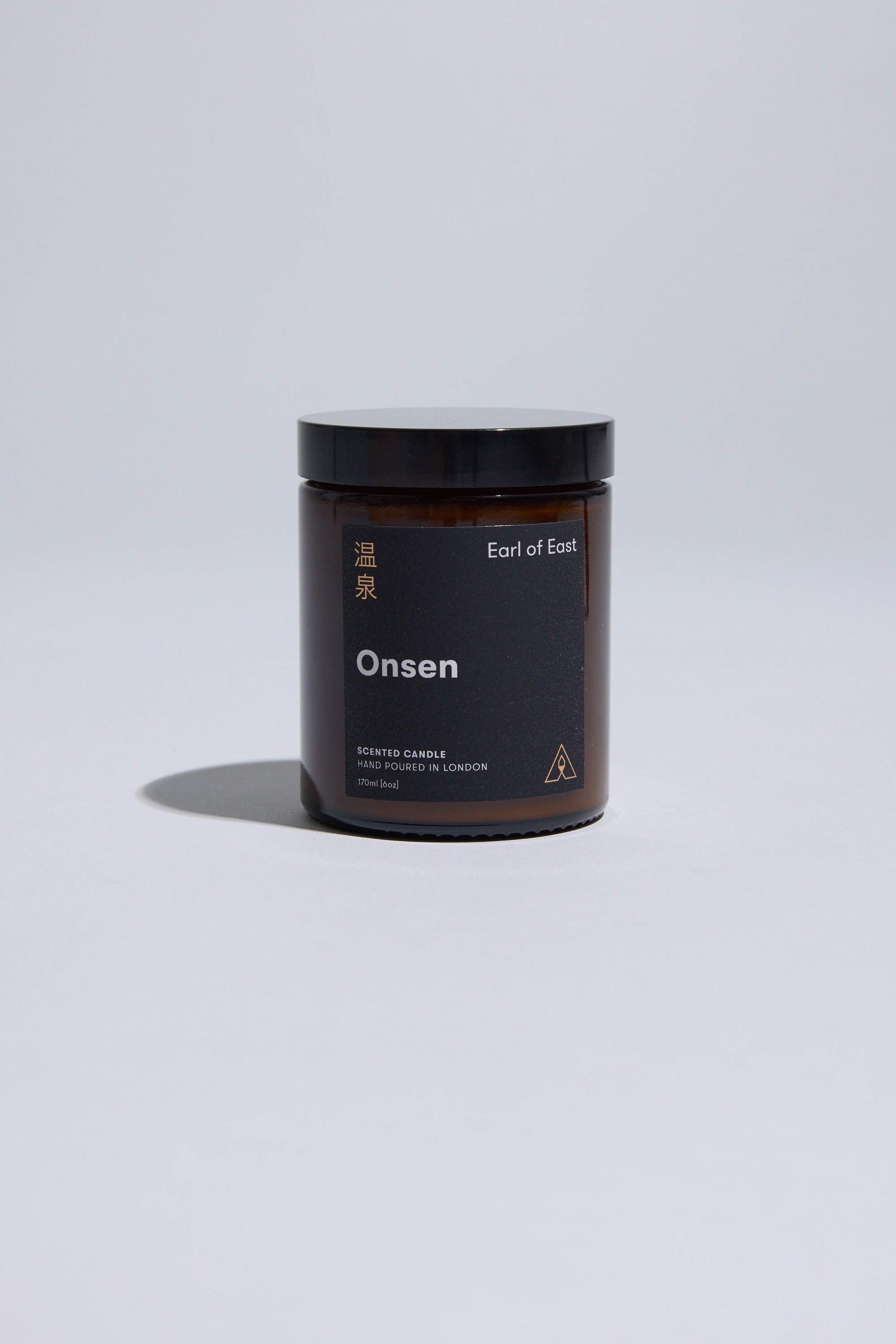 The 170ml EoE Onsen Candle by Earl of East, in a dark amber glass jar with black lid and minimalist gold and white English/Japanese text, is shown against a plain light gray background.