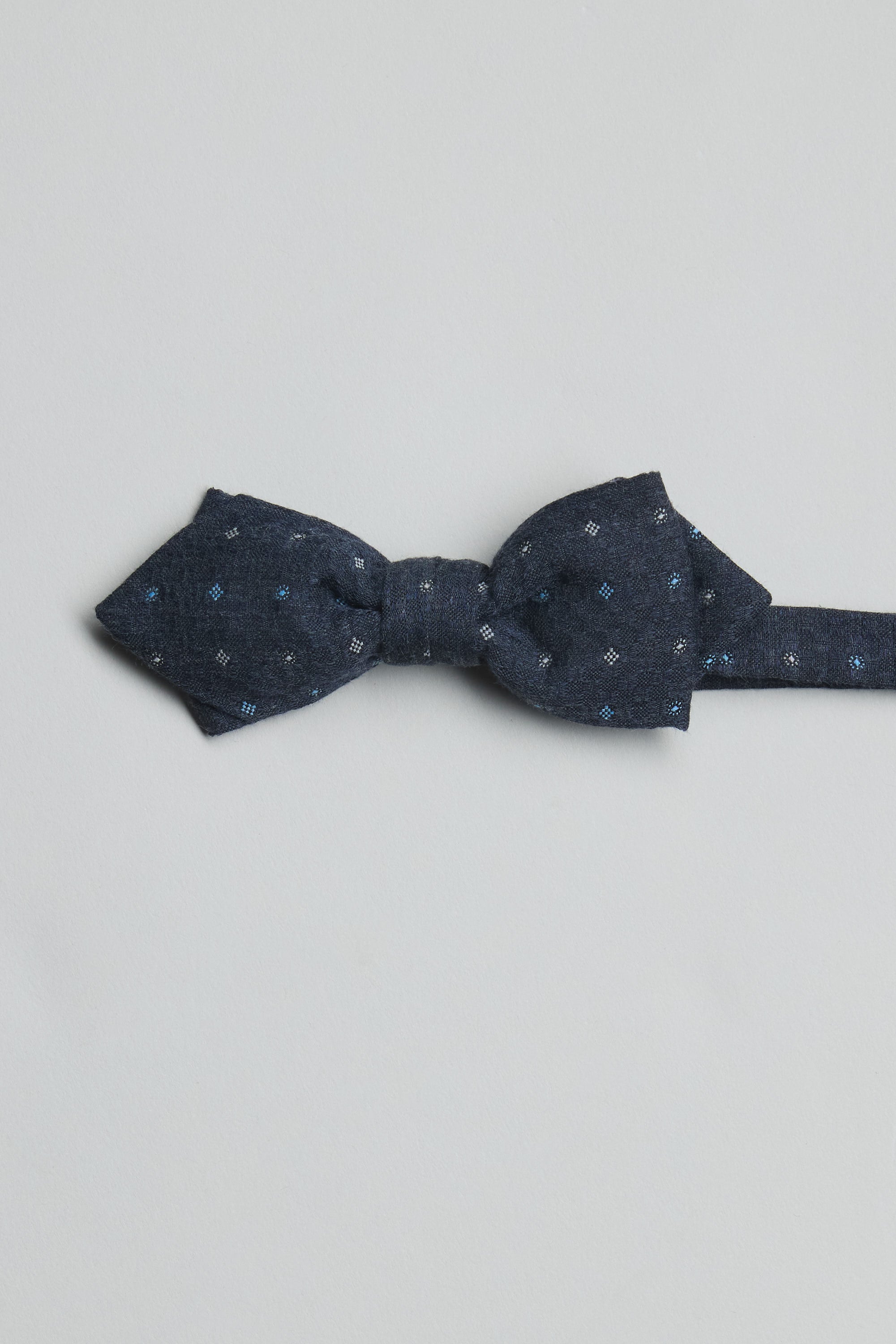 The Parisian Ingram Pattern Bow Tie by Parisian features a dark blue geometric design with light blue and white dots, is handmade in New Zealand, and is displayed flat on a plain light gray background.