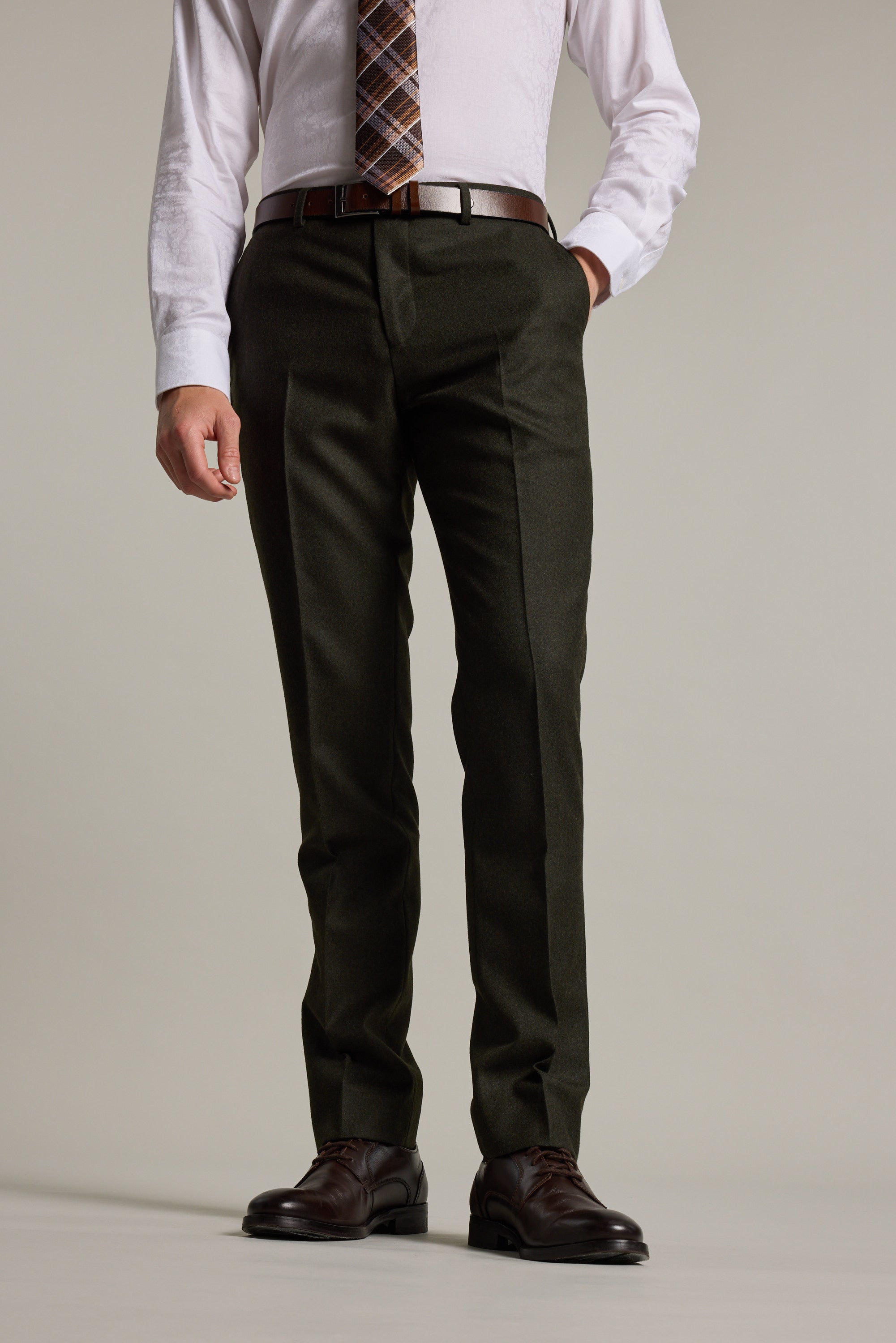 A man models Barkers Howard Suit Trouser, paired with a white dress shirt, patterned tie, and brown dress shoes. He stands with one hand in his pocket against a plain background. His head is not visible in the image.