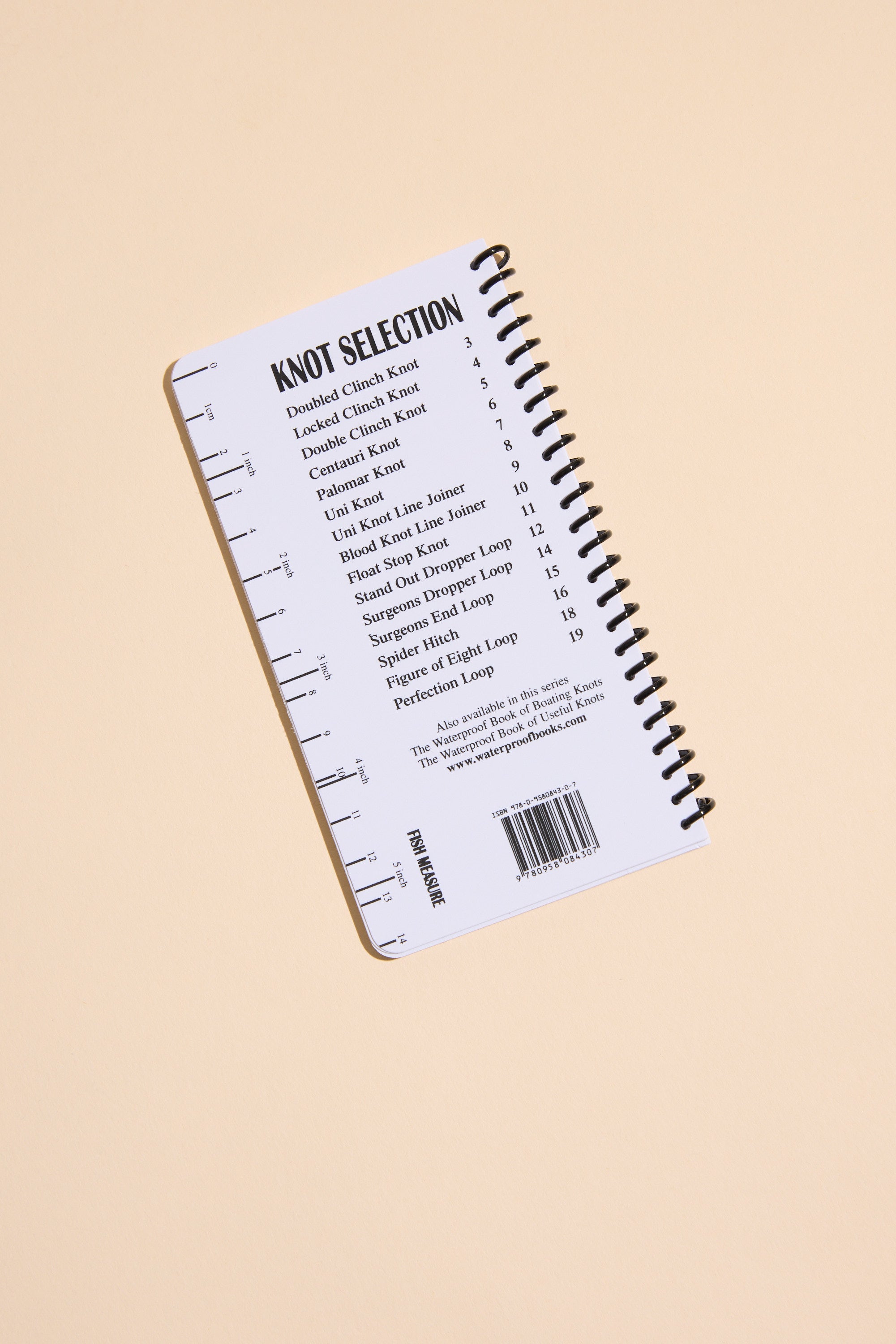 A compact spiral-bound book titled "Fishing Knots" by Other is displayed on a light beige background, featuring top fishing knots and their page numbers on the back cover, plus a printed ruler along the left edge.