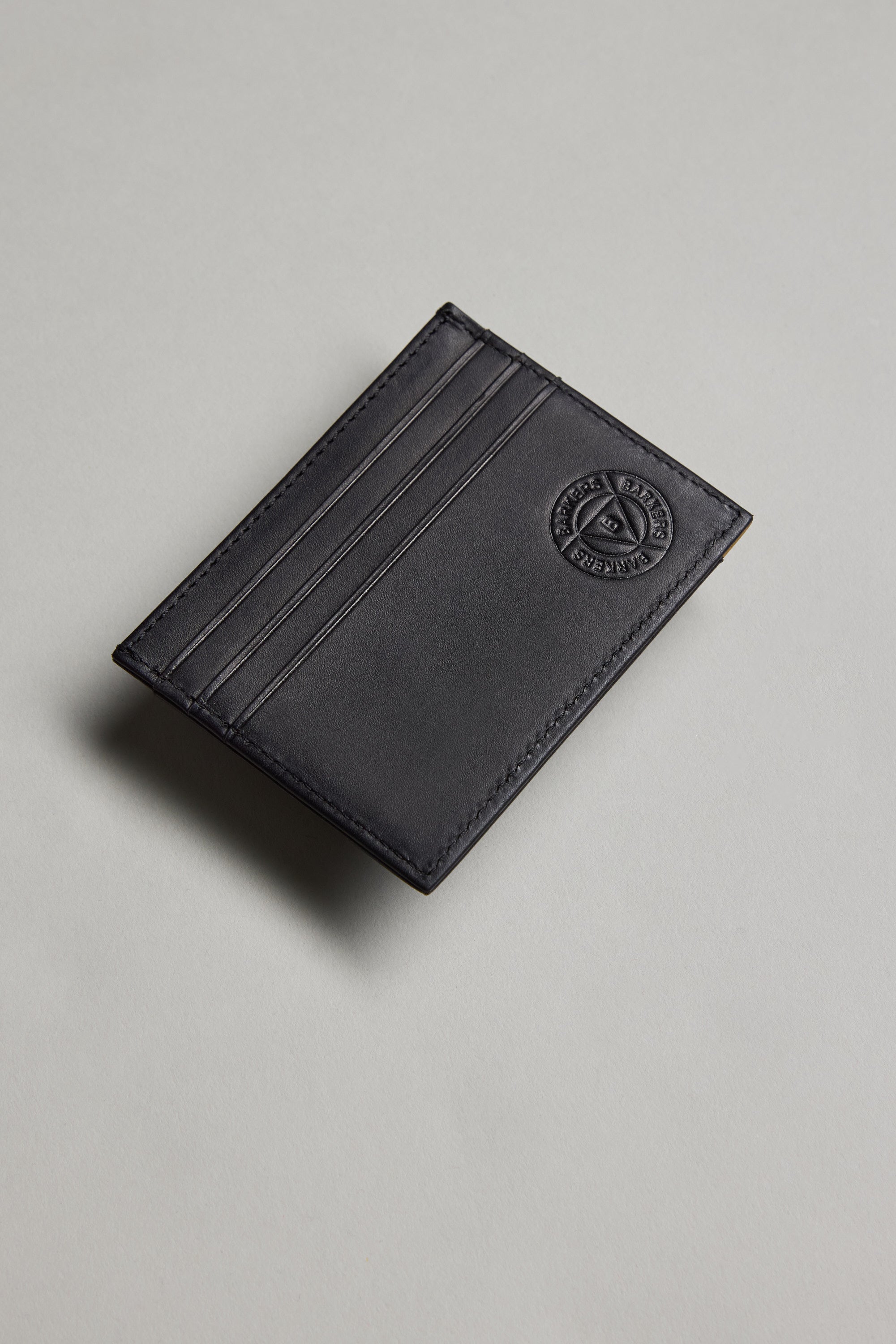 The Barkers Taylor Leather Card Wallet, made from black leather with three slots and an embossed circular logo in the top right corner, is displayed on a light grey surface.