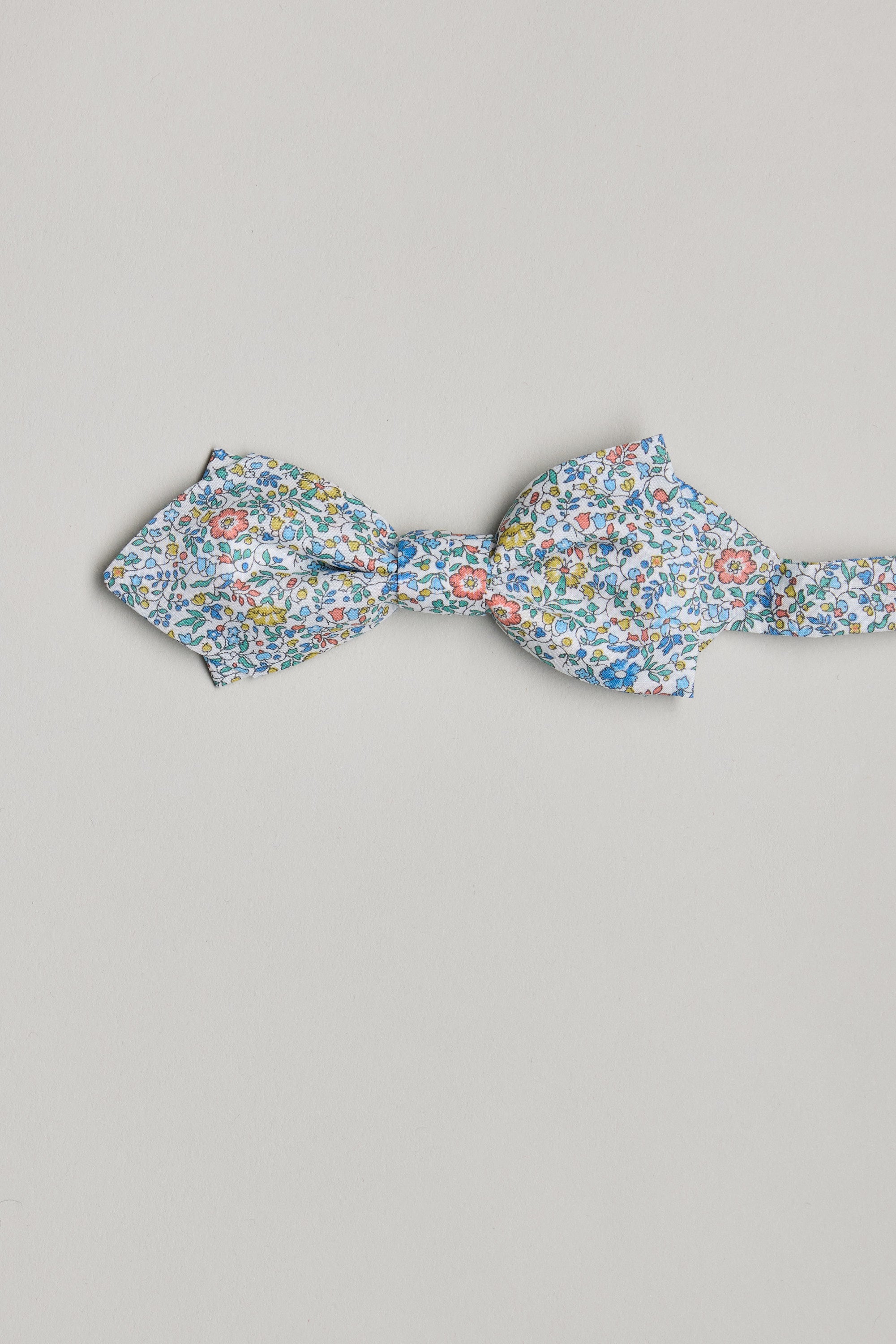 The Katie and Millie Liberty Bow by Liberty features a blue, yellow, and red floral pattern on luxurious Tana Lawn cotton, handmade in New Zealand and shown against a light gray background.