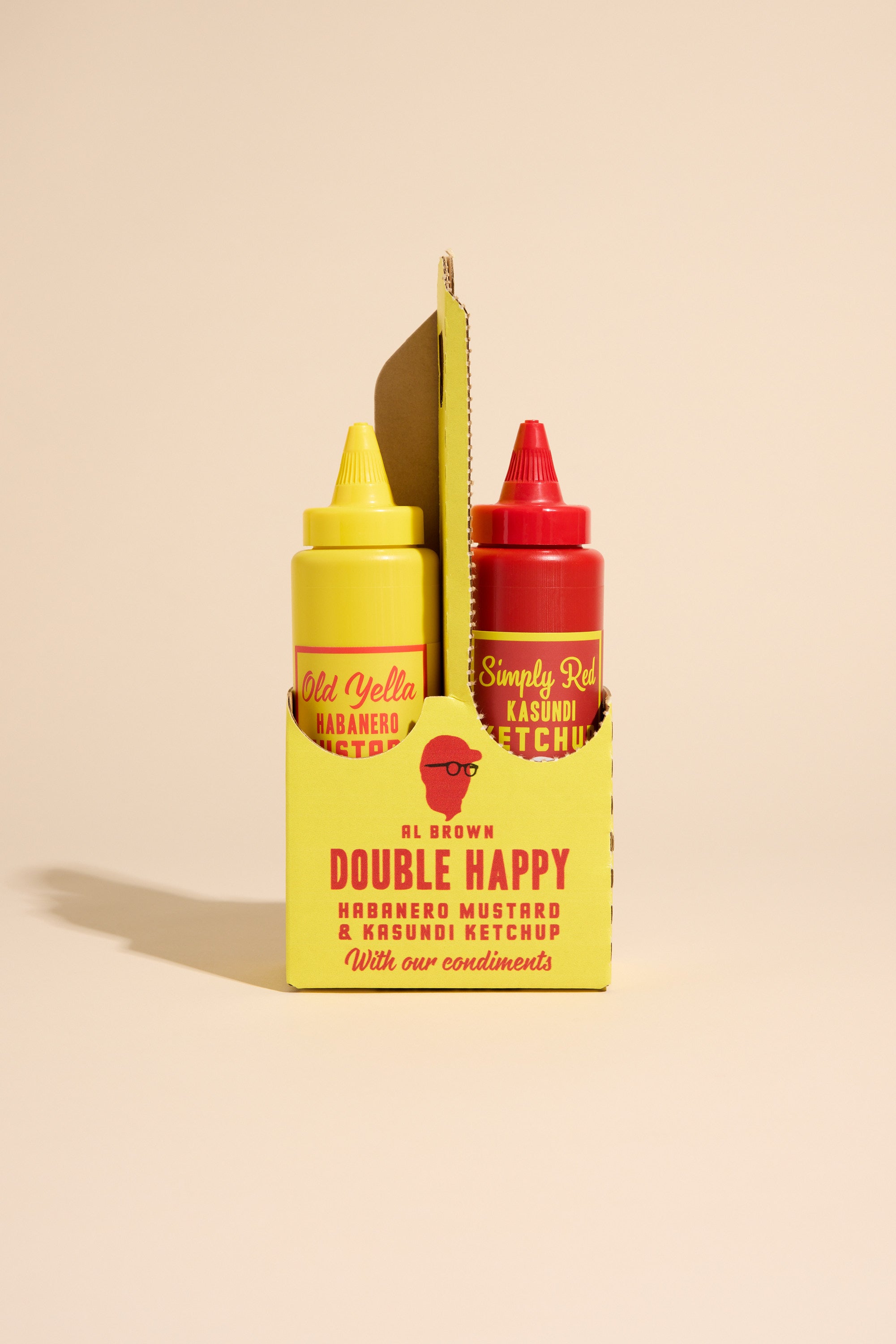 The Old Yella & Simply Red Sauce Caddy by Al's holds two sauces in yellow and red bottles, displayed in a cardboard holder labeled “Double Happy” against a beige background.